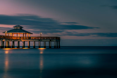 Built structure by sea against sky at sunset