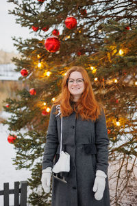 Portrait of young woman standing against christmas tree