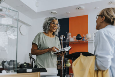 Senior female entrepreneur with credit card reader talking to customer at checkout counter