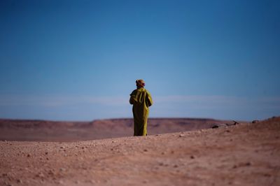 Rear view of man standing in desert against clear sky