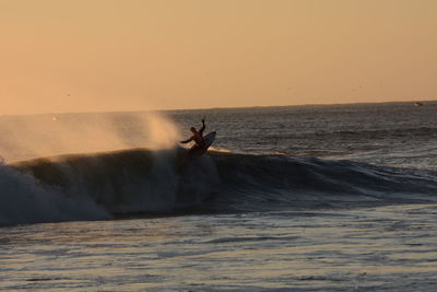 Silhouette man surfing in sea against clear sky during sunset