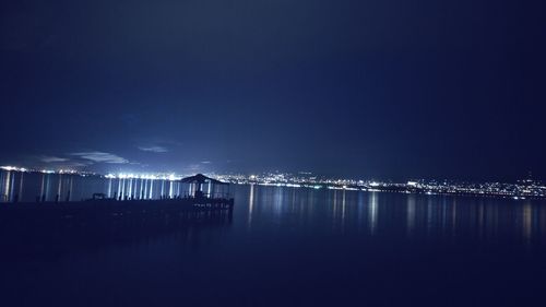 Illuminated pier over sea against sky at night