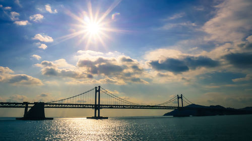 View of suspension bridge over river against cloudy sky