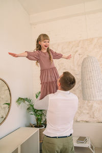 Full length of woman with arms raised standing against wall