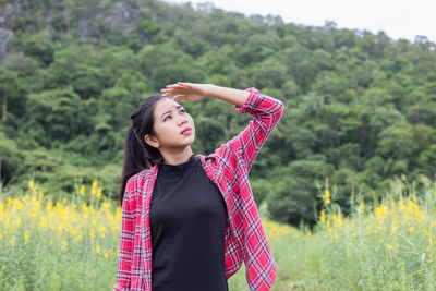 Young woman looking away while standing on field