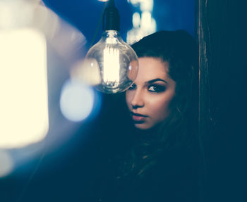 Portrait of young woman by illuminated light bulb in darkroom