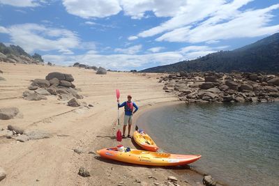 Man standing with kayaks and oar at shore of embalse del burguillo