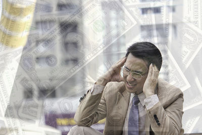 Double exposure of businessman suffering from headache with paper currency