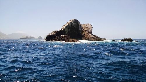 Rock formation in sea against clear blue sky