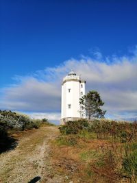 Lighthouse on field by building against sky