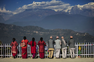 Rear view of people looking at mountains against sky