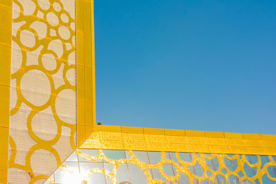 Low angle view of yellow building against clear blue sky