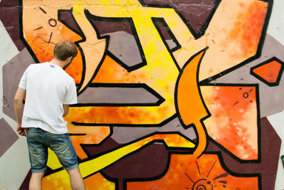 Young man spray painting wall in city