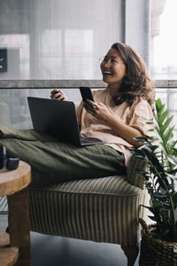 Female computer programmer with laptop and smart phone laughing in office