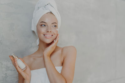 Smiling young woman applying moisturizer at home