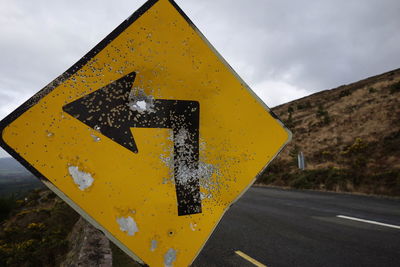 Close-up of arrow sign on road against sky