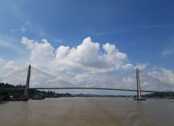 Suspension bridge over river against cloudy sky