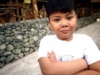 Close-up portrait of boy with arms crossed while standing on footpath at park