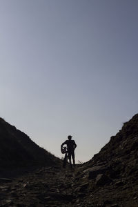 Low angle view of man walking with bicycle on mountain against clear sky