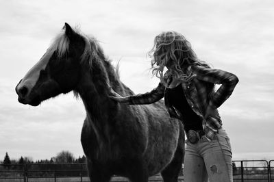 Low angle view of woman petting horse against sky