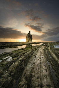 Scenic view of rocks on beach against sky during sunset