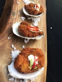 High angle view of fried oysters with aioli served on the half-shell on a rustic wooden board. 