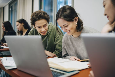 Smiling teenage students studying at desk in school