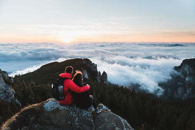 People sitting on rock looking at mountains against sky during sunset