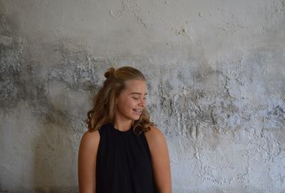 Young woman looking away while standing against wall