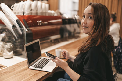 Adult confident serious smiling business woman working in a coffee shop cafe using technology 