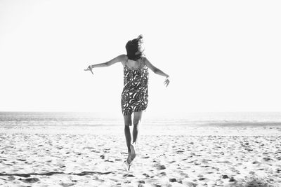 Rear view of excited woman jumping over sandy beach during sunny day