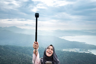 Young woman holding monopod on against mountains
