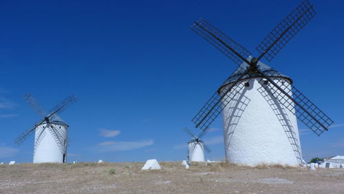 Low angle view of windmills on land against blue sky