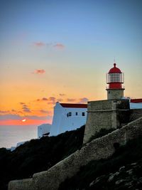 Lighthouse by sea against sky during sunset