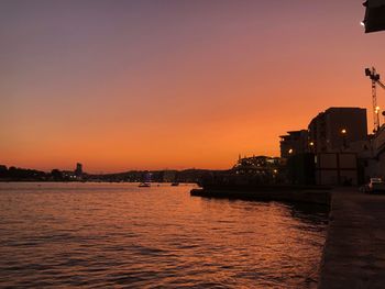 Silhouette buildings by river against romantic sky at sunset