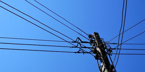 Low angle view of electricity pylon against clear blue sky