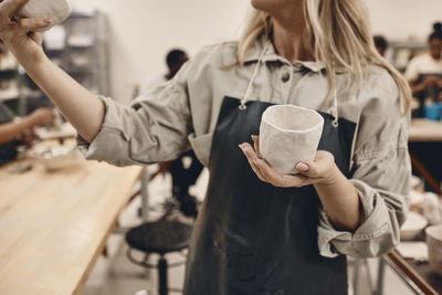 Midsection of mature woman examining ceramics in art class