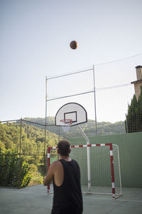 Rear view of man playing basketball hoop against sky