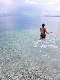 Woman wading in sea against sky