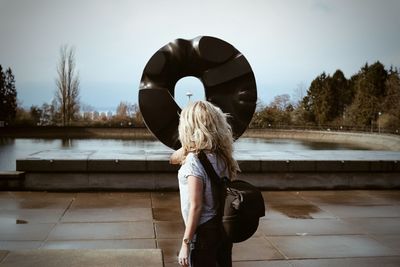 Rear view of woman standing against sculpture by pond