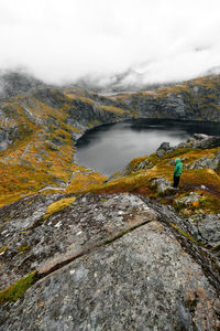 Hiking man at cliff edge with scenic view of lake and mountains at munkebu in lofoten norway