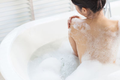 Rear view of topless young woman taking bath in bathtub