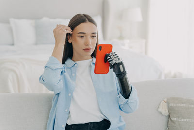 Portrait of young woman using mobile phone while sitting on sofa at home