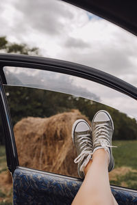 Legs in stylish marsh-colored sneakers in car window, view of an autumn field with haystacks. 