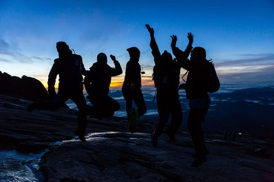 Silhouette friends dancing against sea during sunset