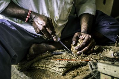 Midsection of man cutting coconut on burlap