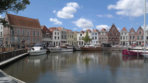 Boats moored in canal by buildings against sky