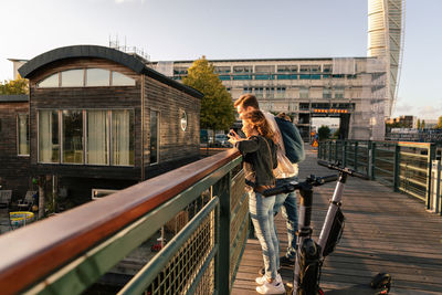 Couple with electric push scooters enjoying on bridge in city against sky