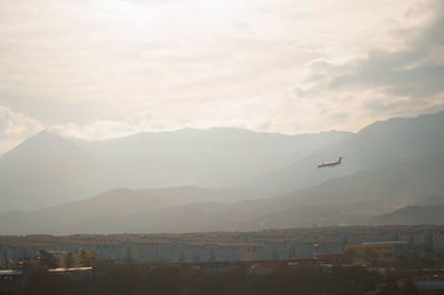 Airplane flying over cityscape against sky