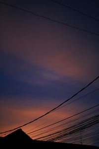 Low angle view of silhouette power lines against sky during sunset